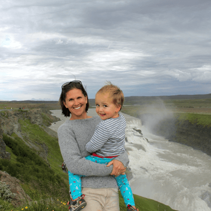 Dark haired smiling mother holding toddler son next to a flowing river.