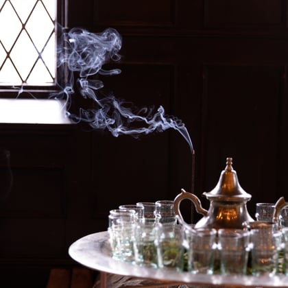 an ornate silver tea pot surrounded by beldi glasses with steam coming from an incense burner