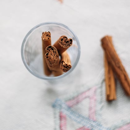 a cup of cinnamon sticks in a clear glass with two laying on a cloth at the side