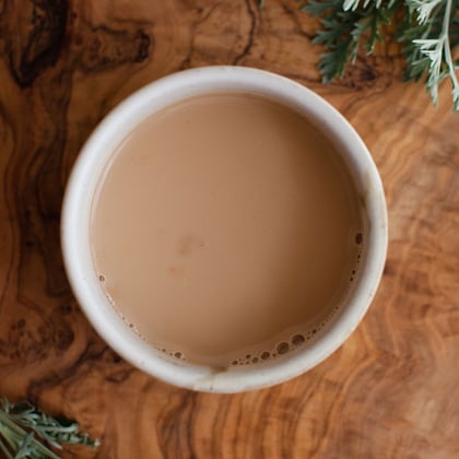 white mug of steaming chai on brown wooden table top decorated with evergreen branches